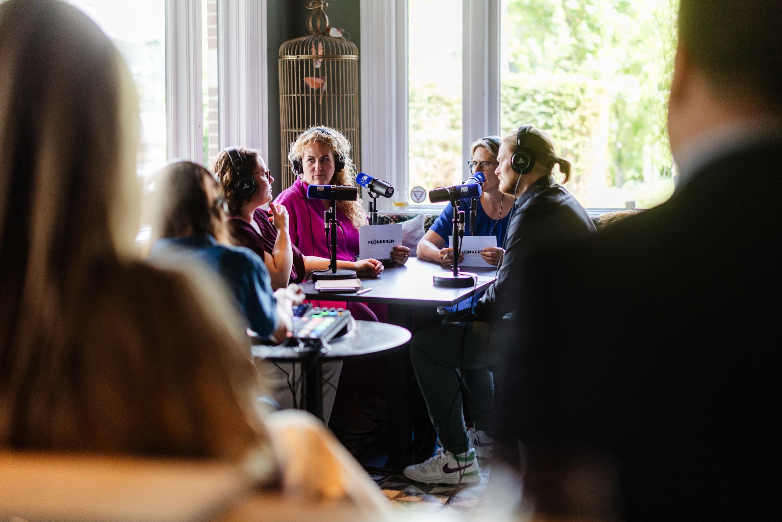 Deelnemers met koptelefoons voeren een podcastgesprek rond een tafel met microfoons